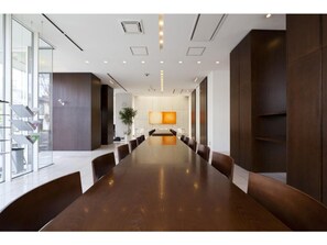 Conference room with a polished table and comfortable seating, featuring a large wall-mounted TV and natural light.