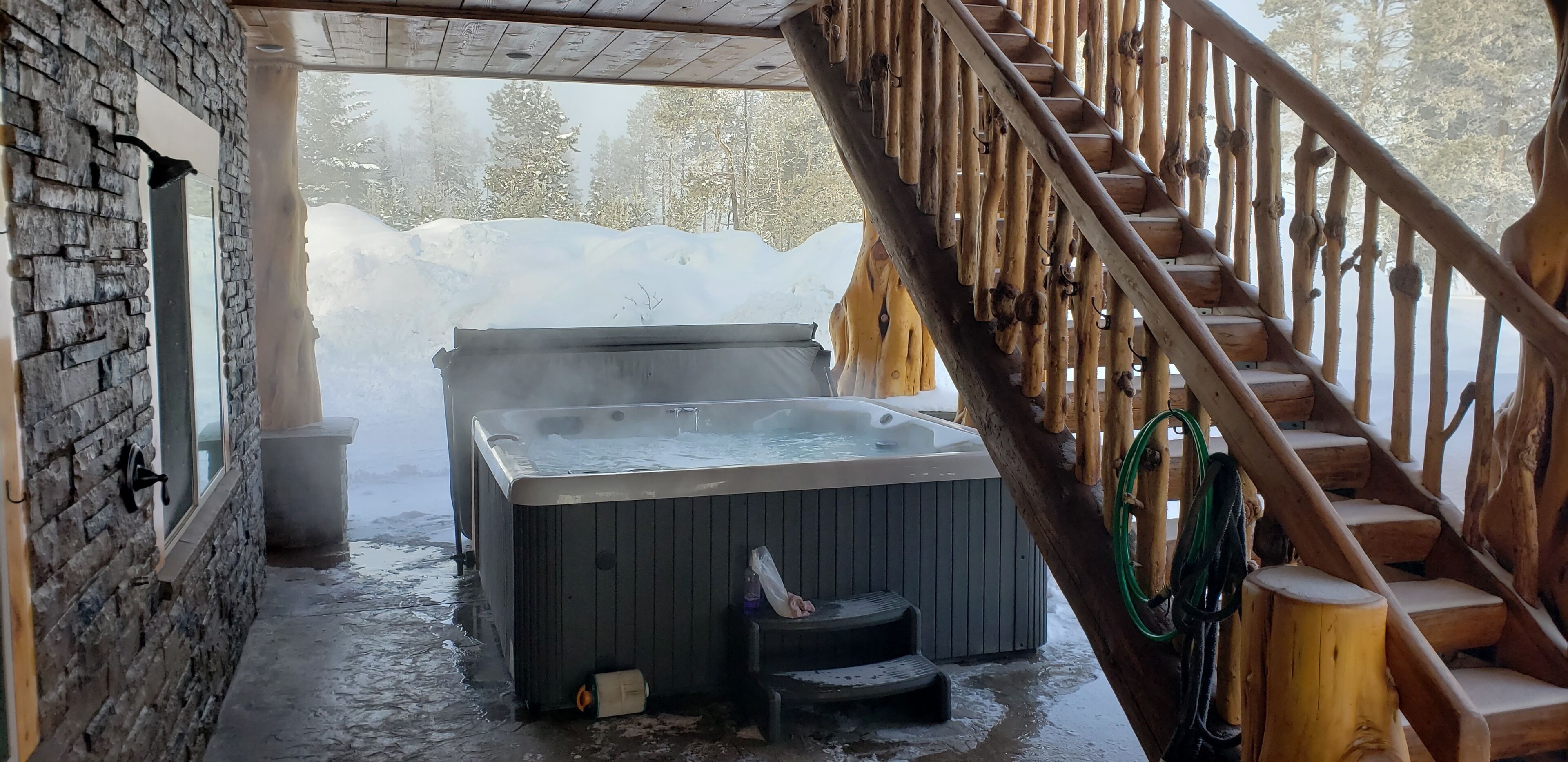 Et rum med stenvægge og en trætrappe op til en jacuzzi.