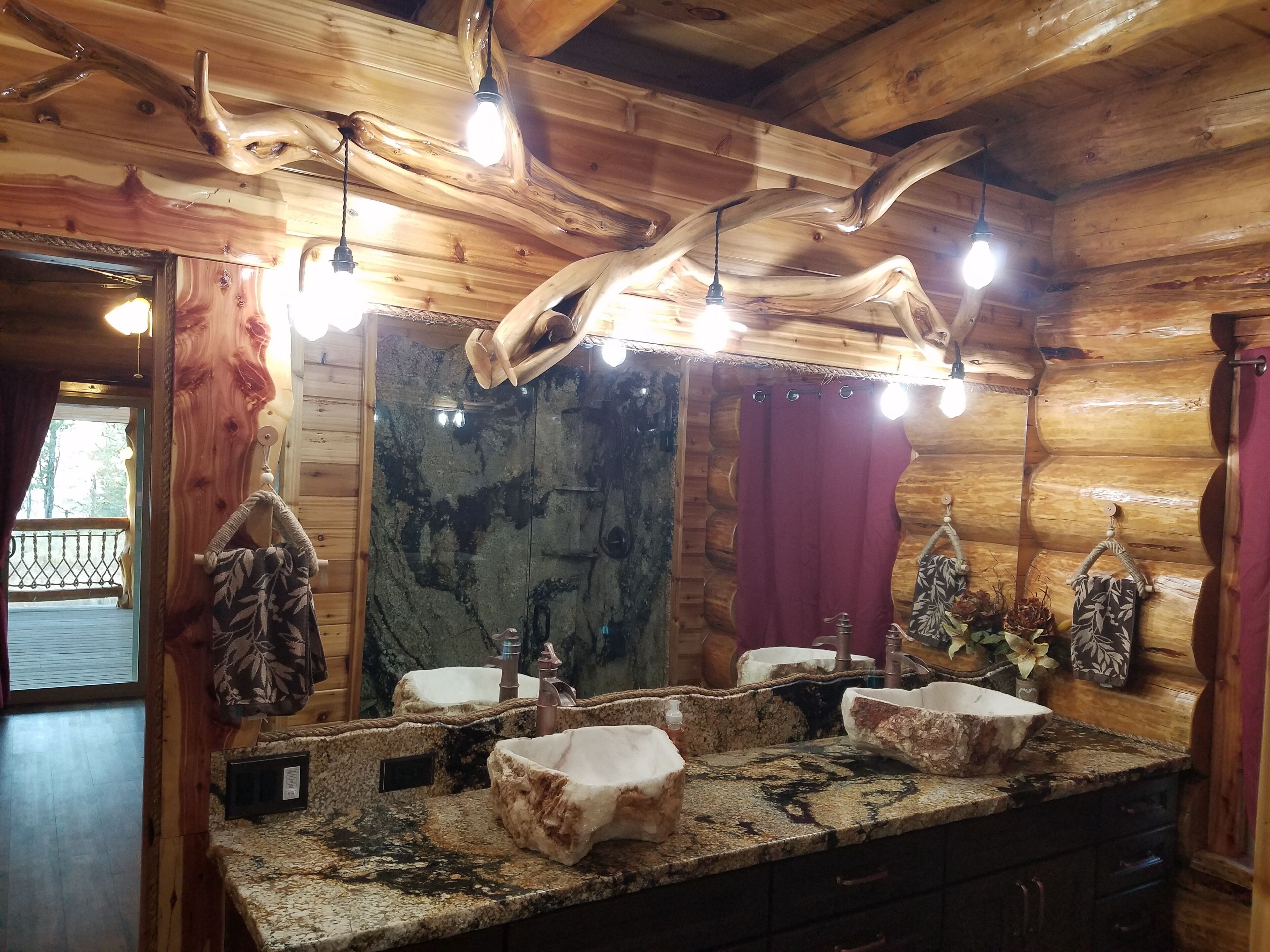 A rustic cabin bathroom with a large mirror, wooden ceiling beams, and a granite countertop.