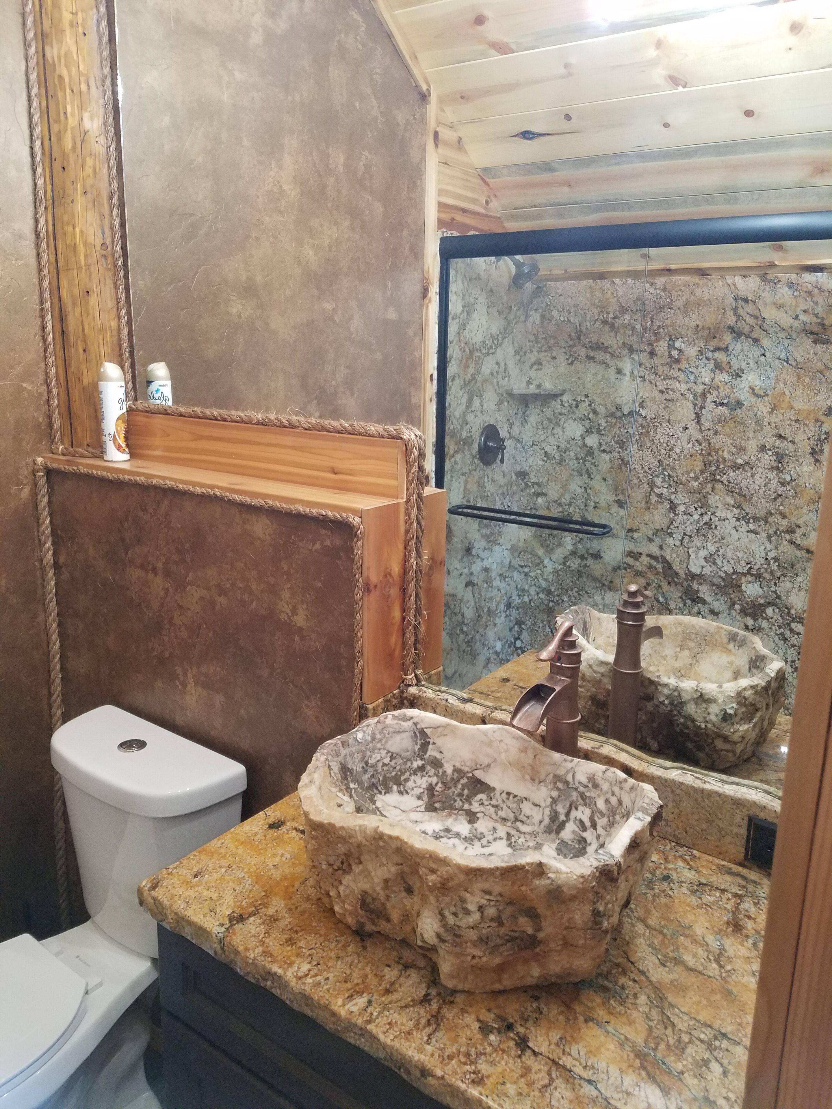 Un baño rústico con lavamanos de piedra, tocador de madera y un inodoro.