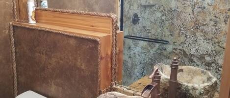 Un baño rústico con lavamanos de piedra, tocador de madera y un inodoro.