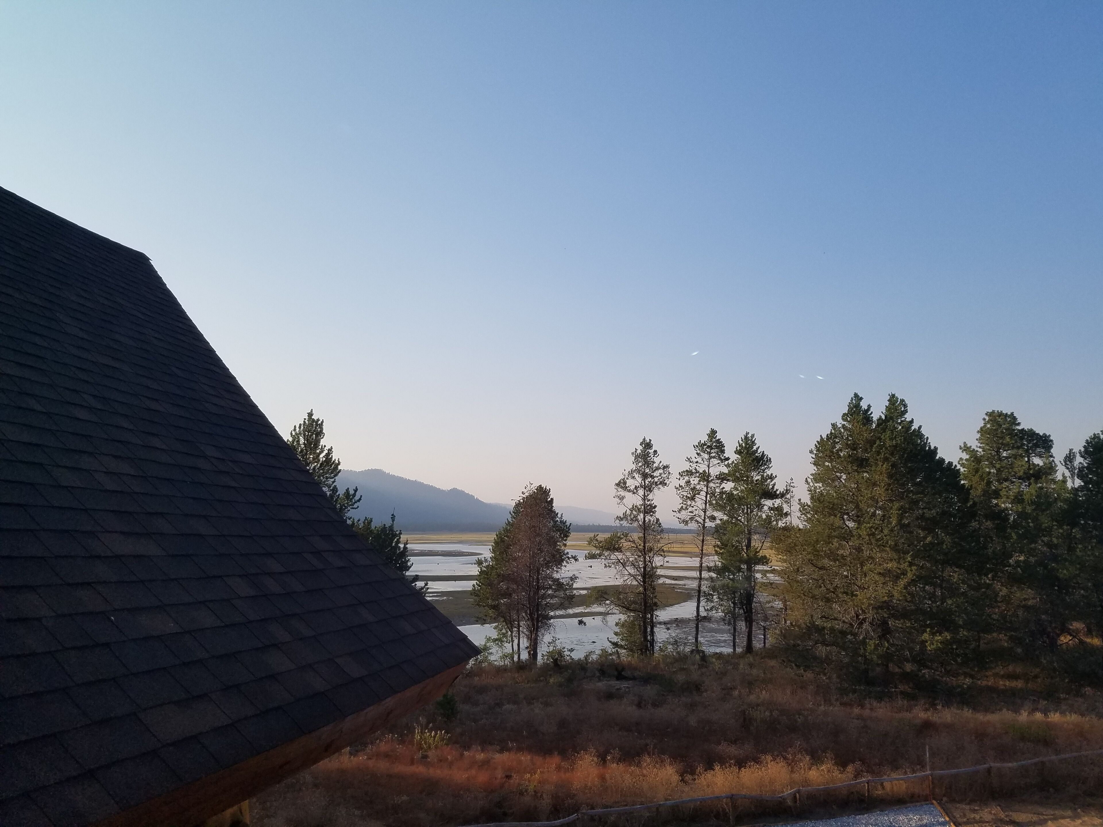 A view of a house with a dark roof, a body of water, and trees in the background.