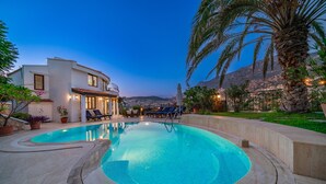 A swimming pool with a curved edge, surrounded by a landscaped area with palm trees and a view of a mountain range.