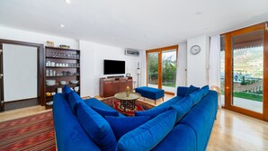 A living room with a blue sofa, a television, a bookshelf, and a view through a glass door.