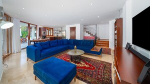 A spacious living area with a large blue sectional sofa, a round coffee table, and a TV on a wooden stand.