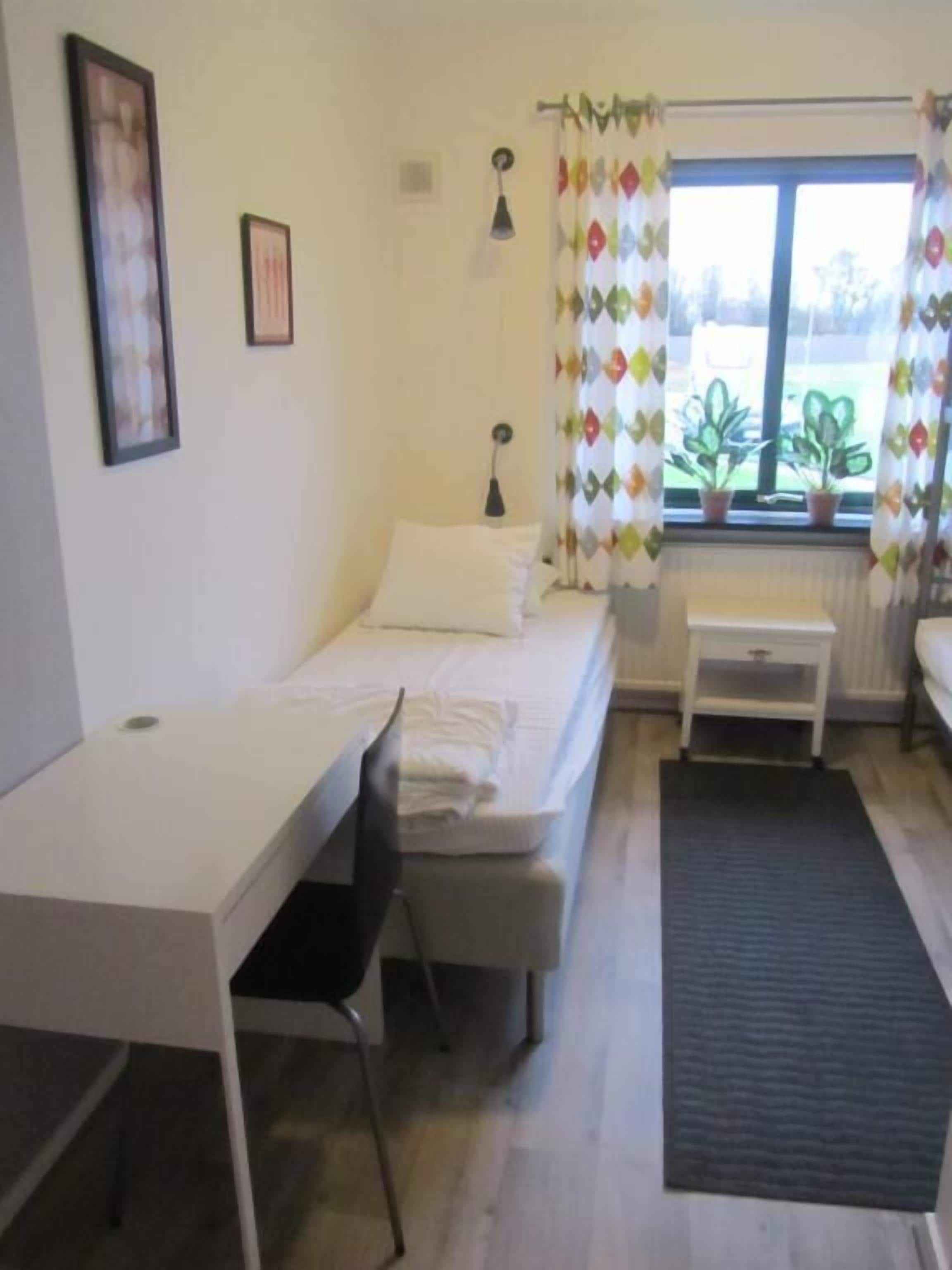 A small, clean room with a bed, a desk, and a window with curtains.