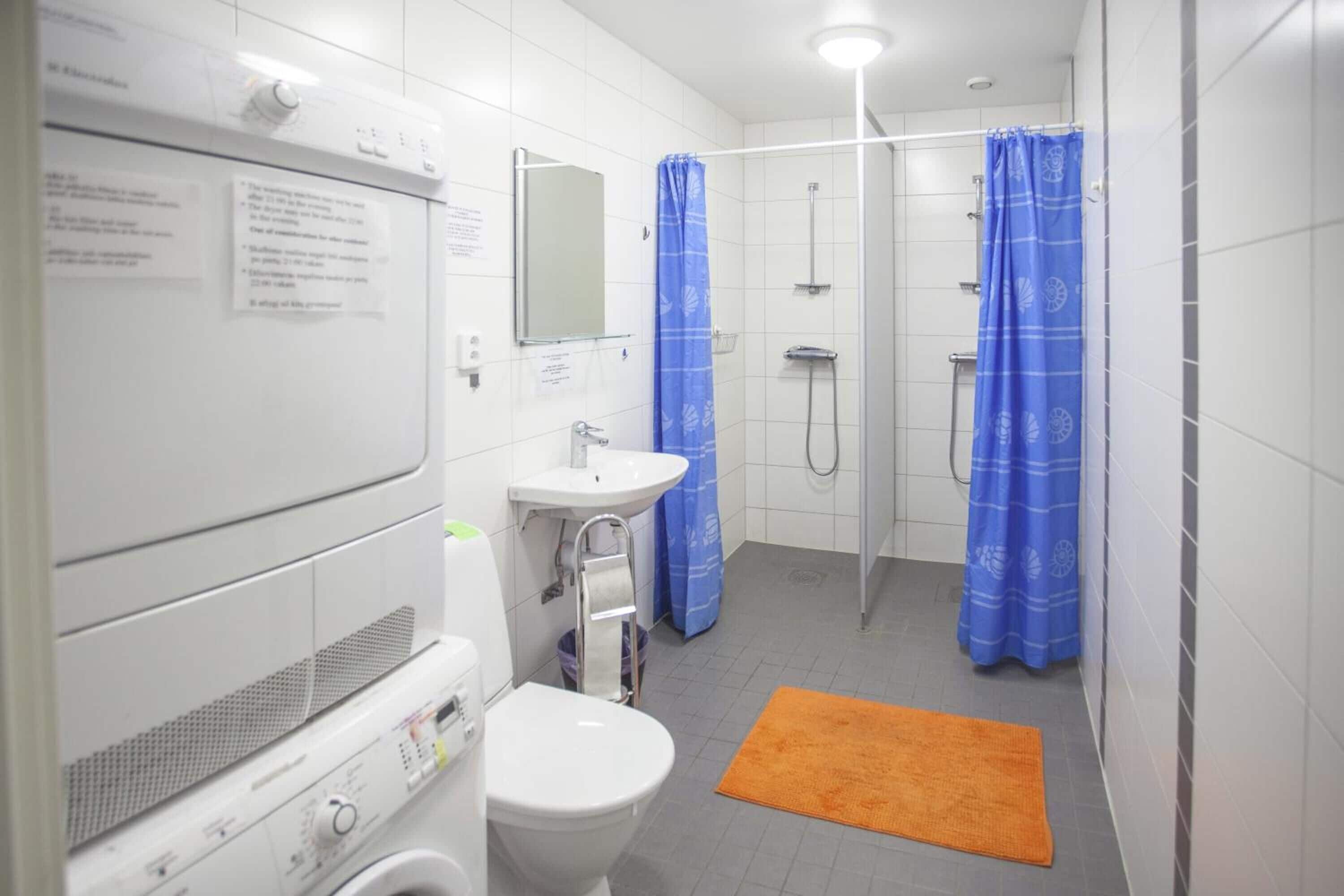 A bathroom with a washing machine, a sink, a toilet, and a shower area with blue curtains.