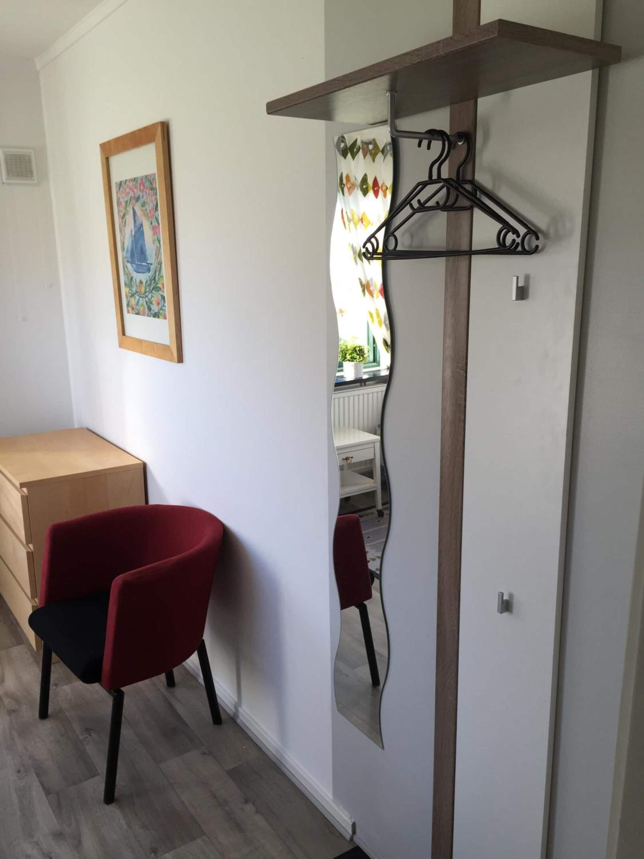 A room with a red chair, a wooden cabinet, and a mirror with a hanger.