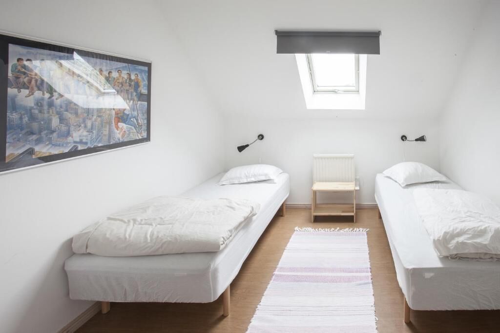 Un dormitorio con dos camas individuales, un tragaluz, un cuadro en la pared y una mesita entre las camas.