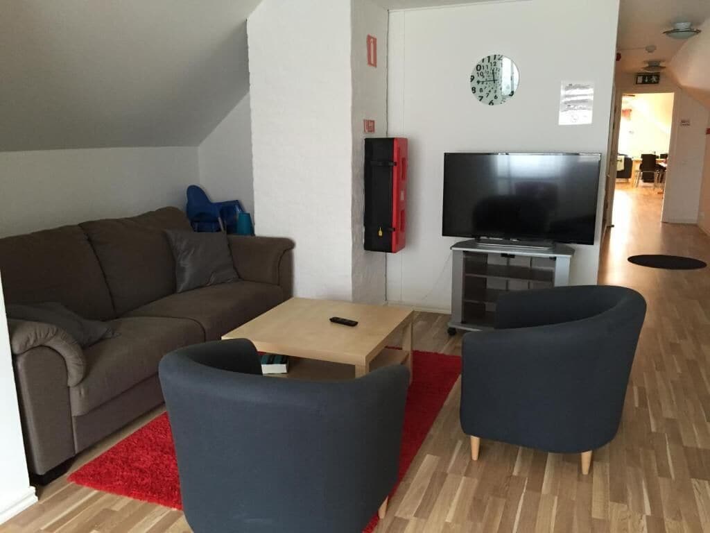 Ein Wohnzimmer mit einer Couch, einem Couchtisch, zwei Sesseln, einem Fernseher und einem roten Teppich.