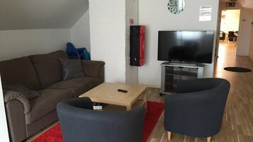 Ein Wohnzimmer mit einer Couch, einem Couchtisch, zwei Sesseln, einem Fernseher und einem roten Teppich.