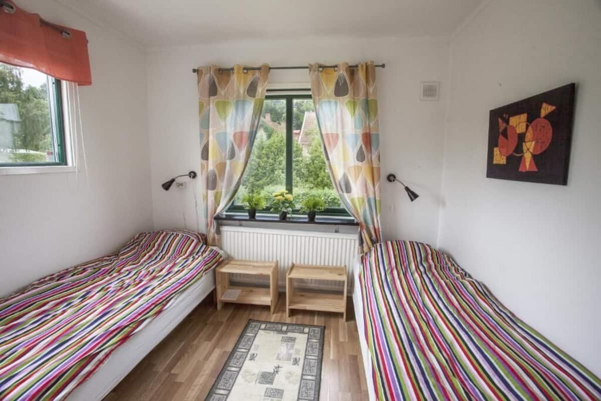 Um quarto pequeno e aconchegante com duas camas de solteiro, uma janela com cortinas, um radiador e uma mesinha.
