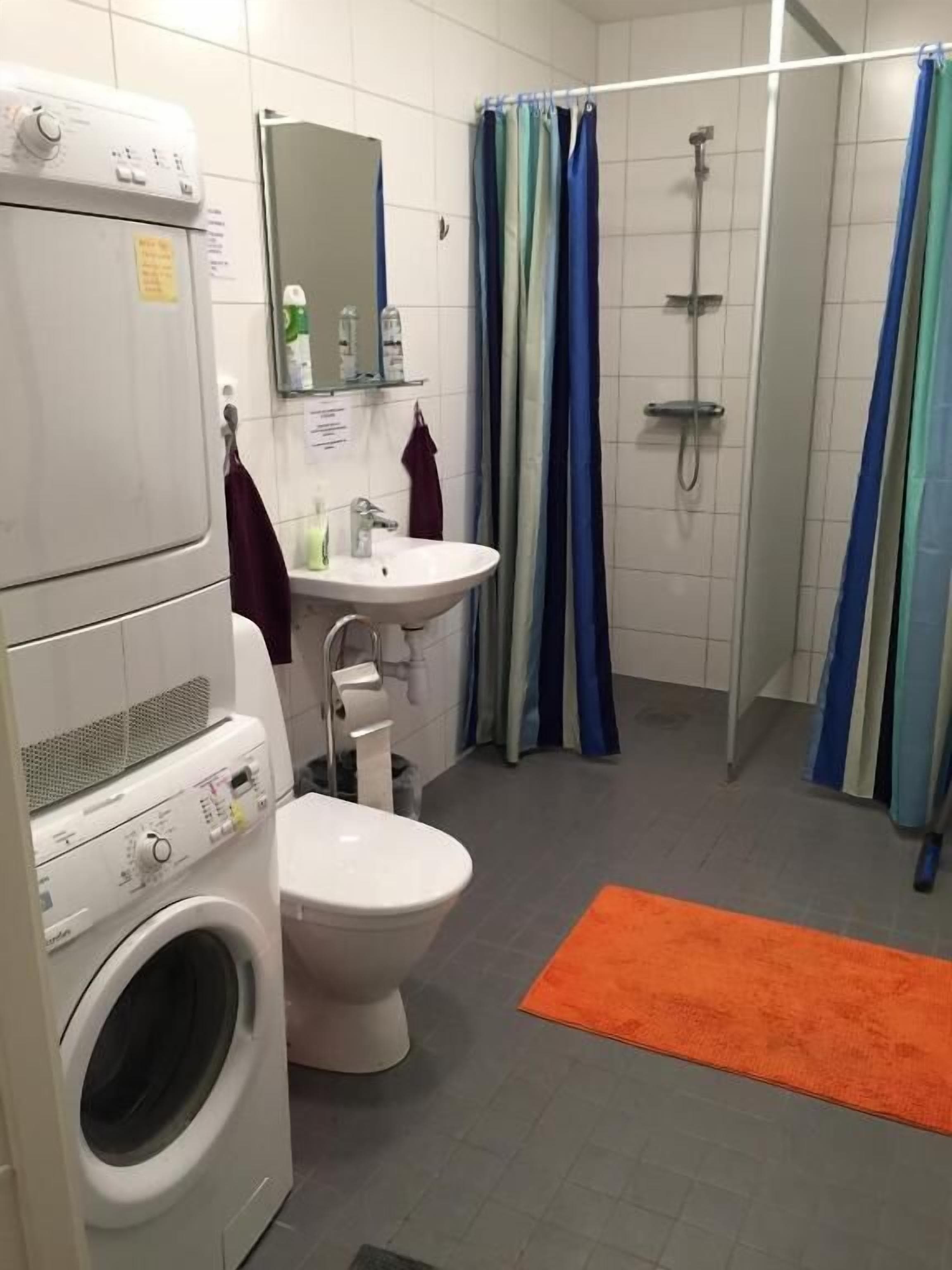 Une petite salle de bain équipée d’un lave-linge, de toilettes, d’un lavabo et d’une douche.