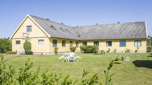 Un edificio giallo con tetto spiovente, un piccolo giardino con tavolo e sedie bianche e un cielo azzurro intenso.