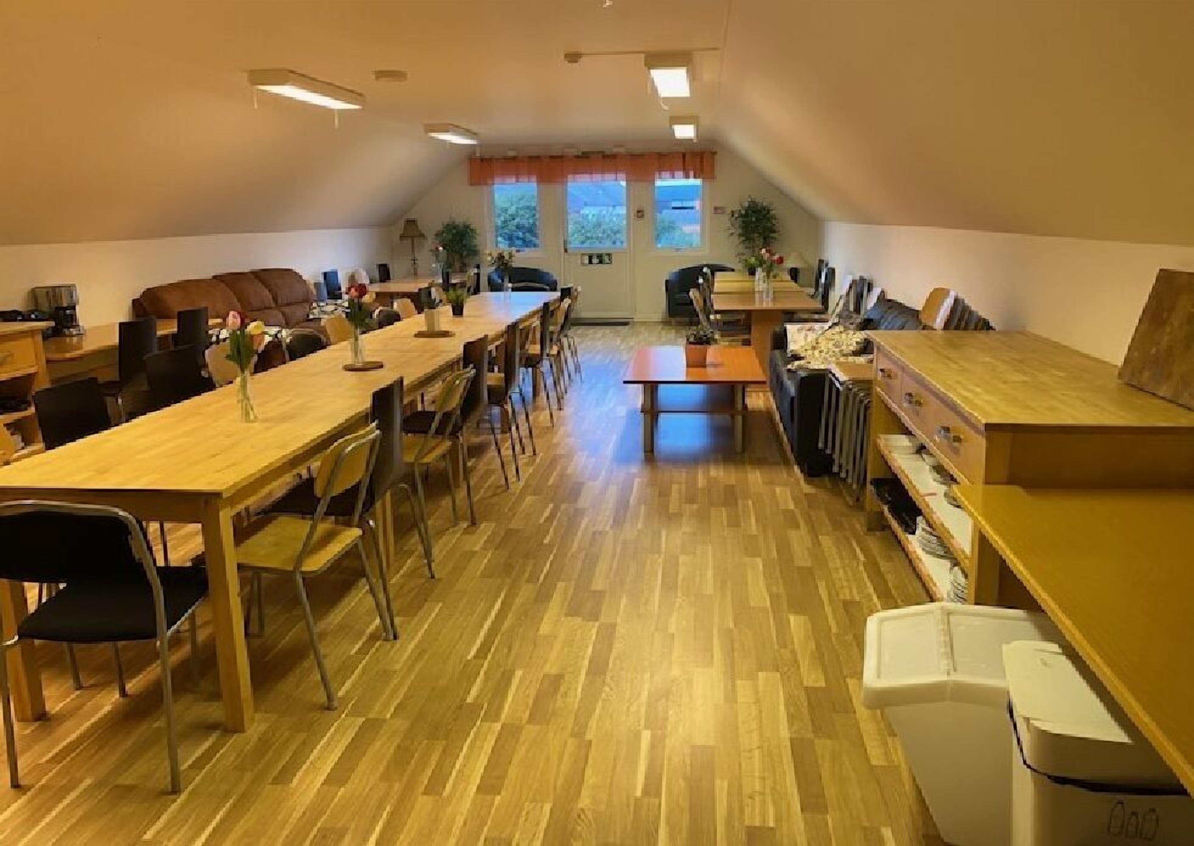 Una habitación amplia con una larga mesa de madera, varias sillas, un sofá y un radiador.