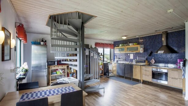 Una cucina moderna con una scala a chiocciola centrale, pavimento in legno e un'area pranzo con una scacchiera.