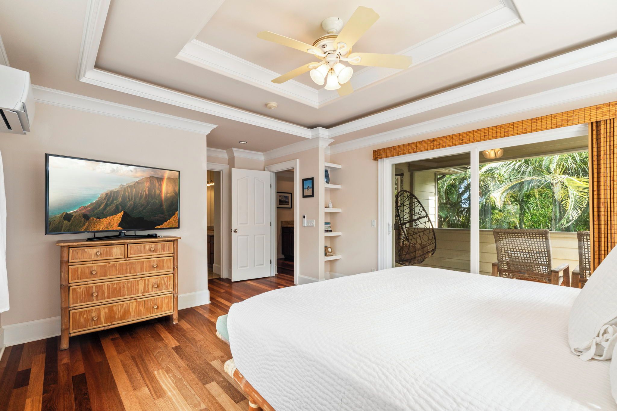 A bedroom with a large bed, a television, a wooden dresser, and a ceiling fan.