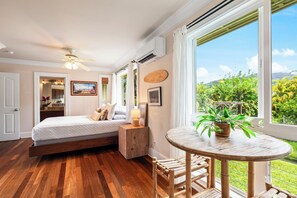 Ein Schlafzimmer mit einem Bett, einem Nachttisch, einem Sessel, einem runden Tisch und Blick auf Grünfläche.