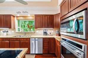 Cozinha moderna com armários de madeira, eletrodomésticos de aço inoxidável e uma janela com vista para o verde.
