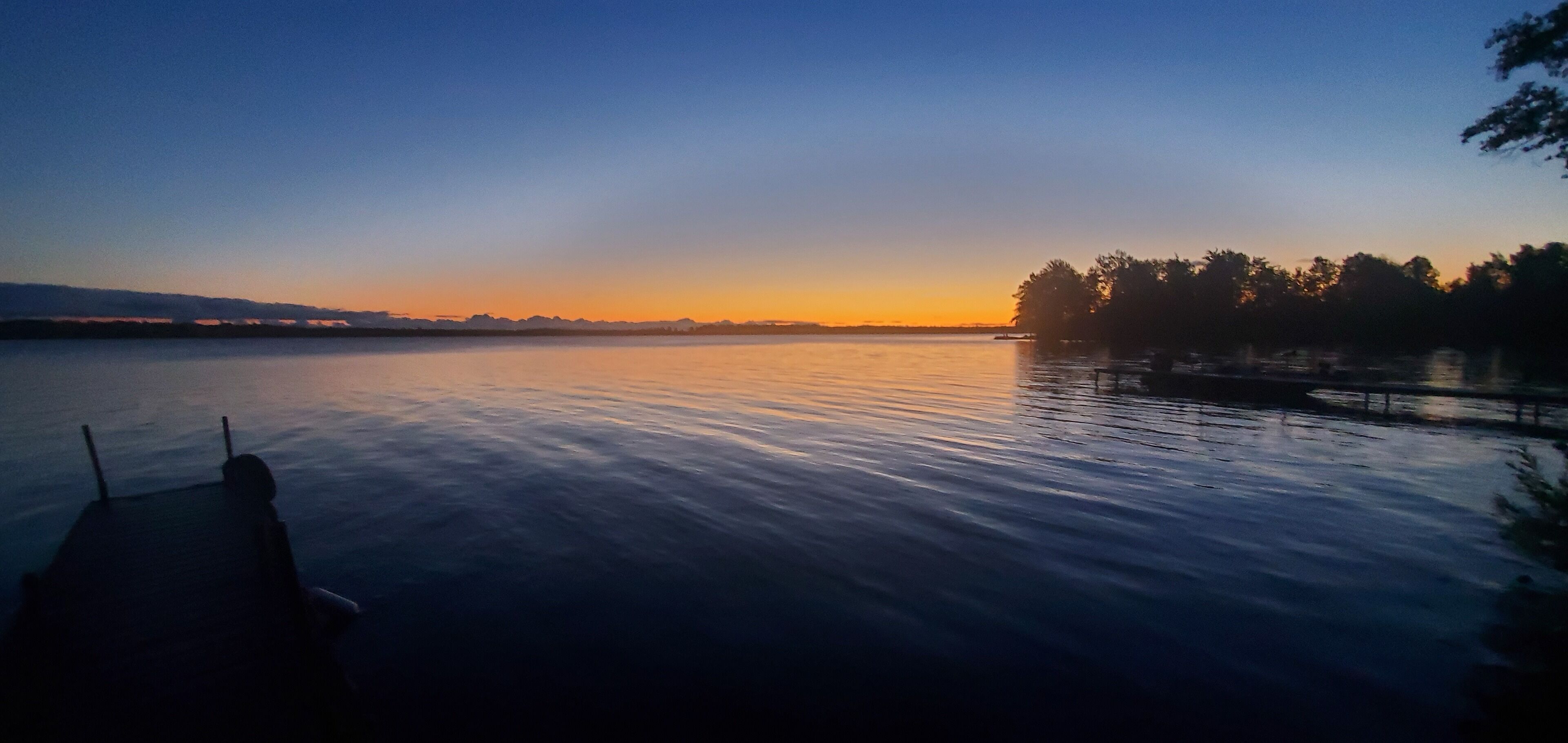A calm lake at sunset with a dock in the foreground.