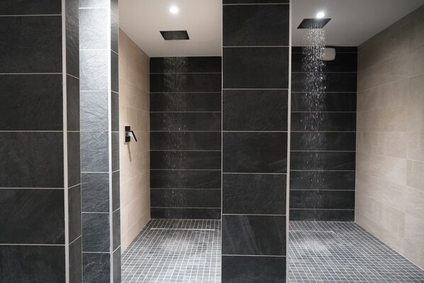 Un box doccia moderno con piastrelle scure e un getto d'acqua visibile.