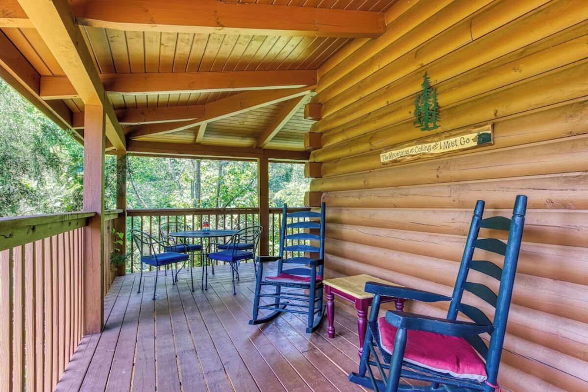 Eine Holzhütte mit überdachter Veranda, Schaukelstühlen und einem kleinen Tisch.