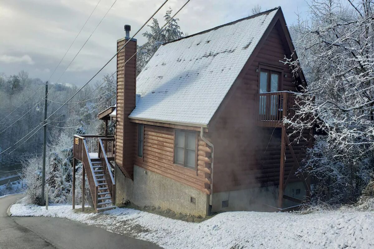 Una cabaña de troncos con fachada de madera, una chimenea y un balcón pequeño.