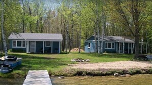 A cabin with a dock extending into a clear stream, surrounded by trees and a grassy area. - Presque Isle Resort, cottage #3 of 3 (Alpena)