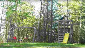 A playground with a slide and climbing structures, surrounded by trees. - Presque Isle Resort, cottage #3 of 3 (Alpena)