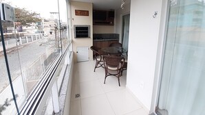 A balcony with a glass door, a dining table with wicker chairs, a hanging light fixture, and a kitchen area with a countertop and cabinets. - 315, Ótimo Apartamento 3 Dormitórios Próximo a Praia (SC)