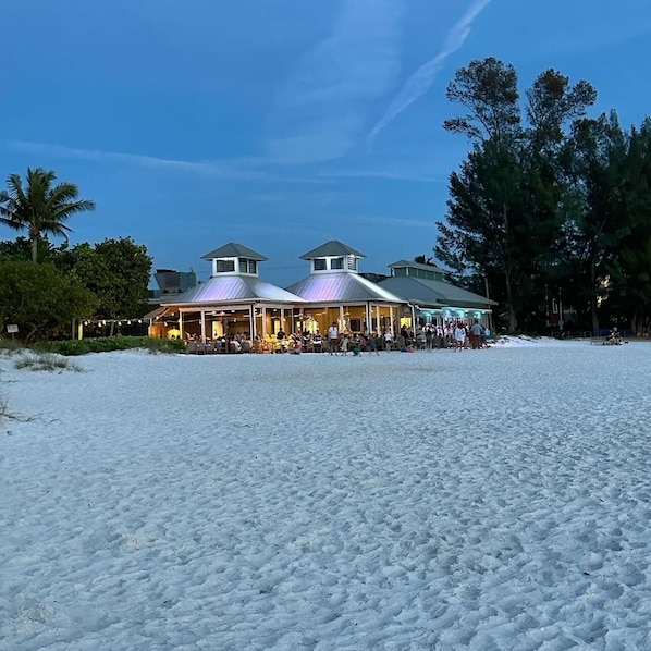 Un bâtiment situé au bord de la plage, doté de plusieurs espaces abrités et d’un parterre sablonneux.