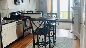 A modern kitchen with white cabinets, a black stove, and a dining area with a patterned rug.
