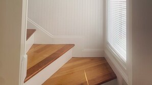 A staircase with wooden steps and white wainscoting, leading to a room with a large window and a framed picture of a bird on the wall.