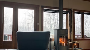 Una habitación acogedora con una chimenea moderna, un sillón confortable y grandes ventanales con vistas al exterior.