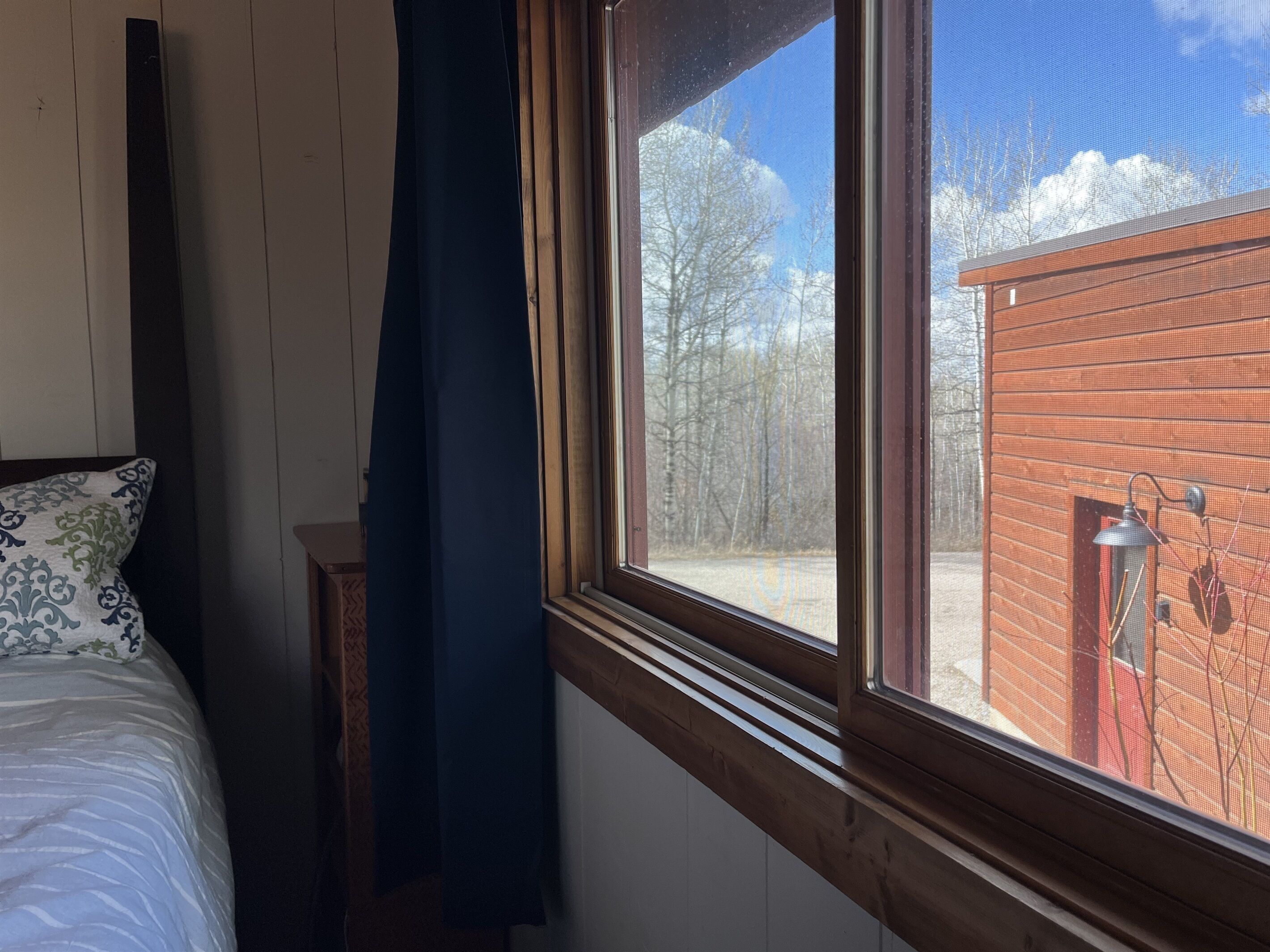 A bedroom with a large window, a bed with patterned pillows, and a view of a red building outside.