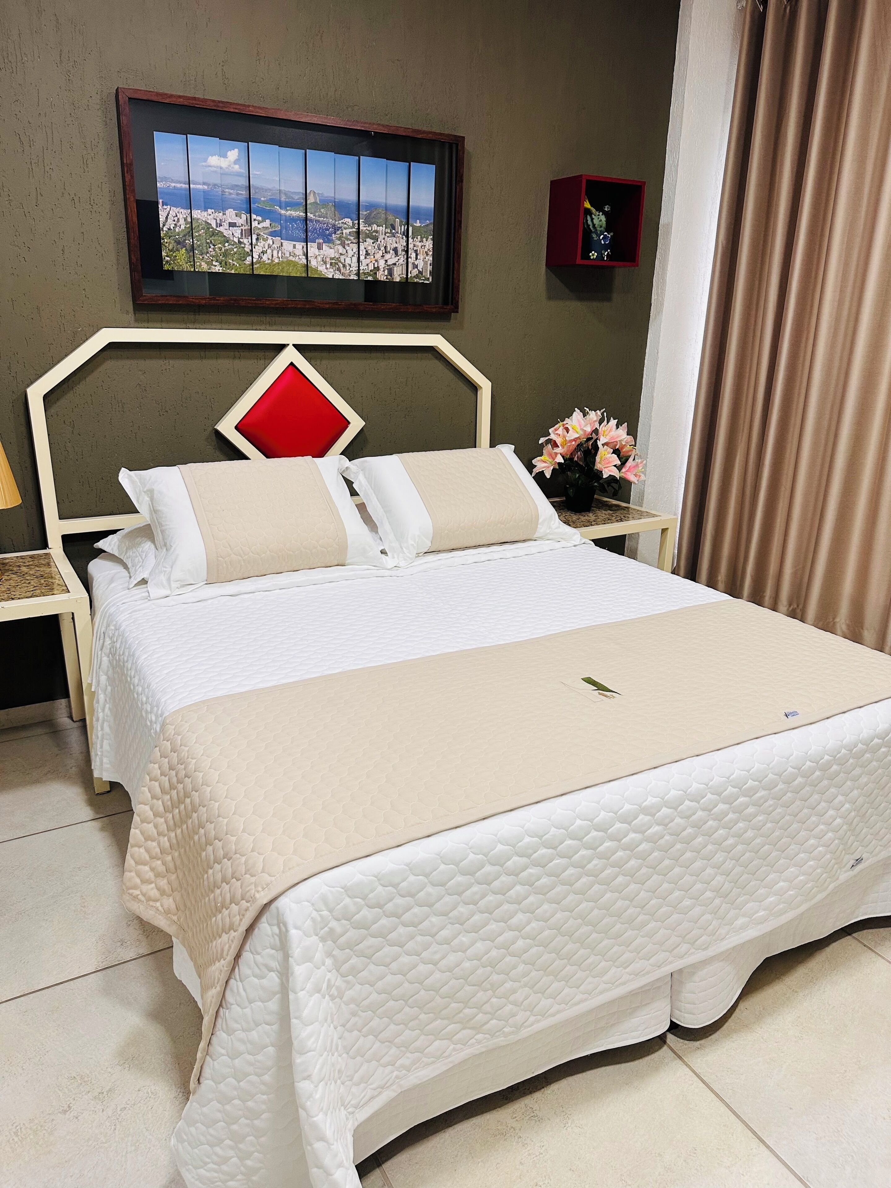 Una cama bien hecha con cubrecolcha blanco acolchado, una almohada decorativa roja y una manta color beige.