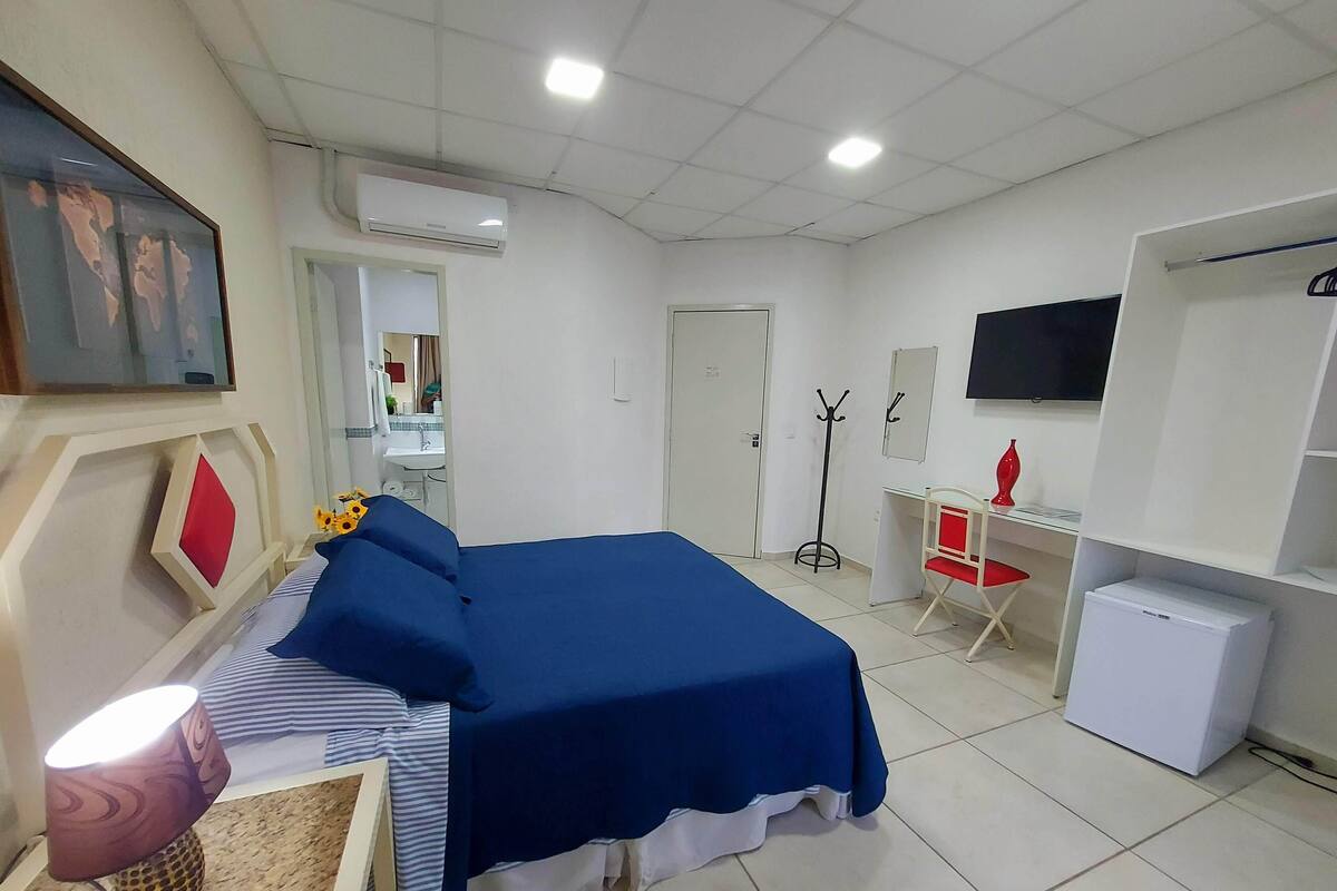 Habitación de hotel con cama, escritorio, silla, televisor y refrigerador pequeño.