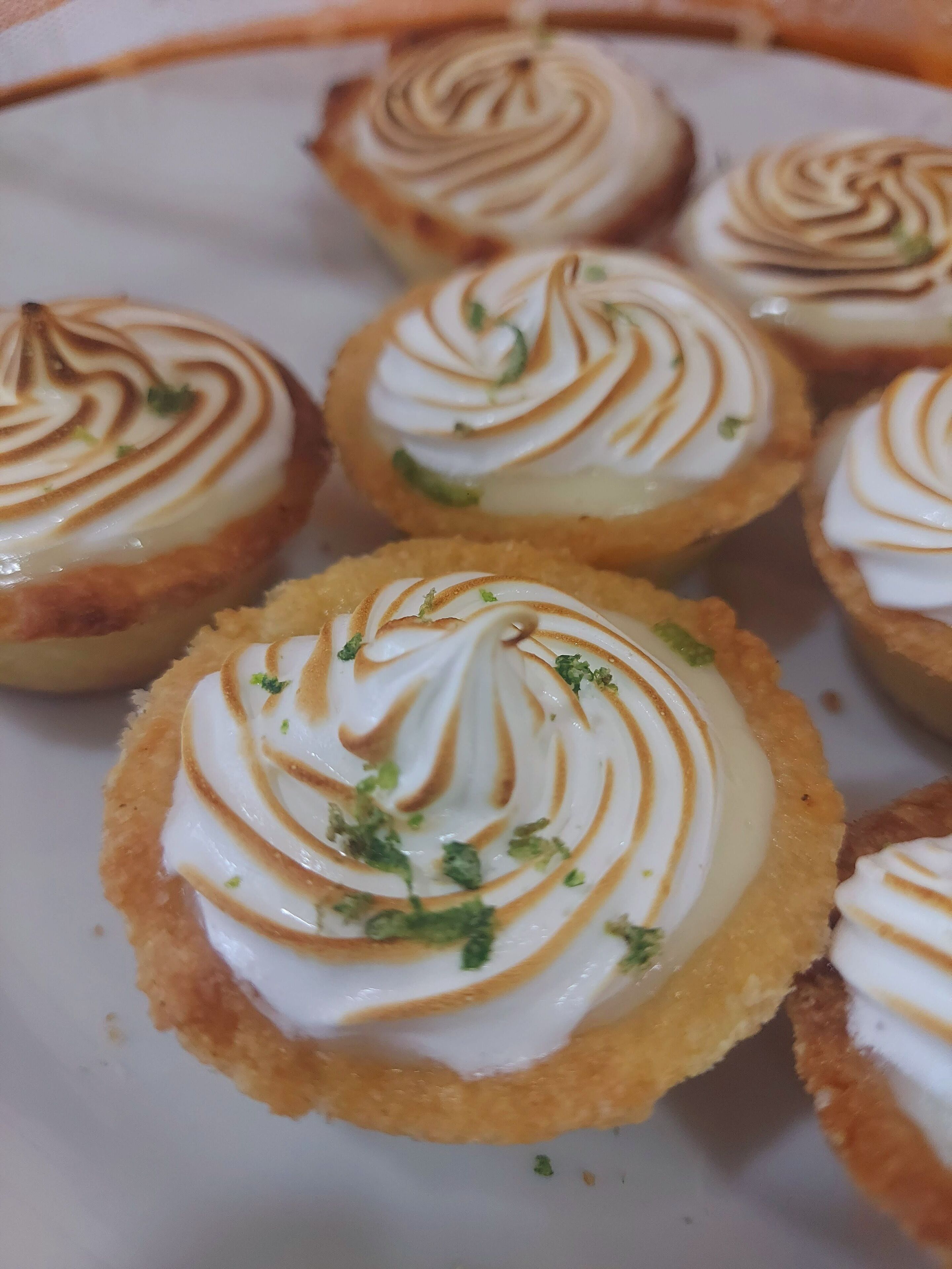 Een bordje met kleine gebakjes, afgetopt met een romige topping en bestrooid met groene kruiden.