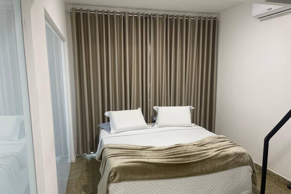 Una habitación de hotel con cama, cortinas, ventana y aire acondicionado.