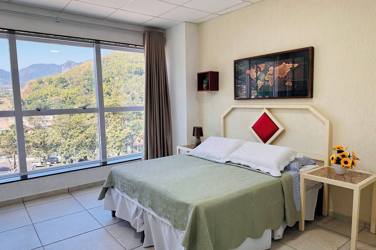 Habitación de hotel con cama, mesita de noche, ventana con vistas a montañas y un mapa mundial en la pared.