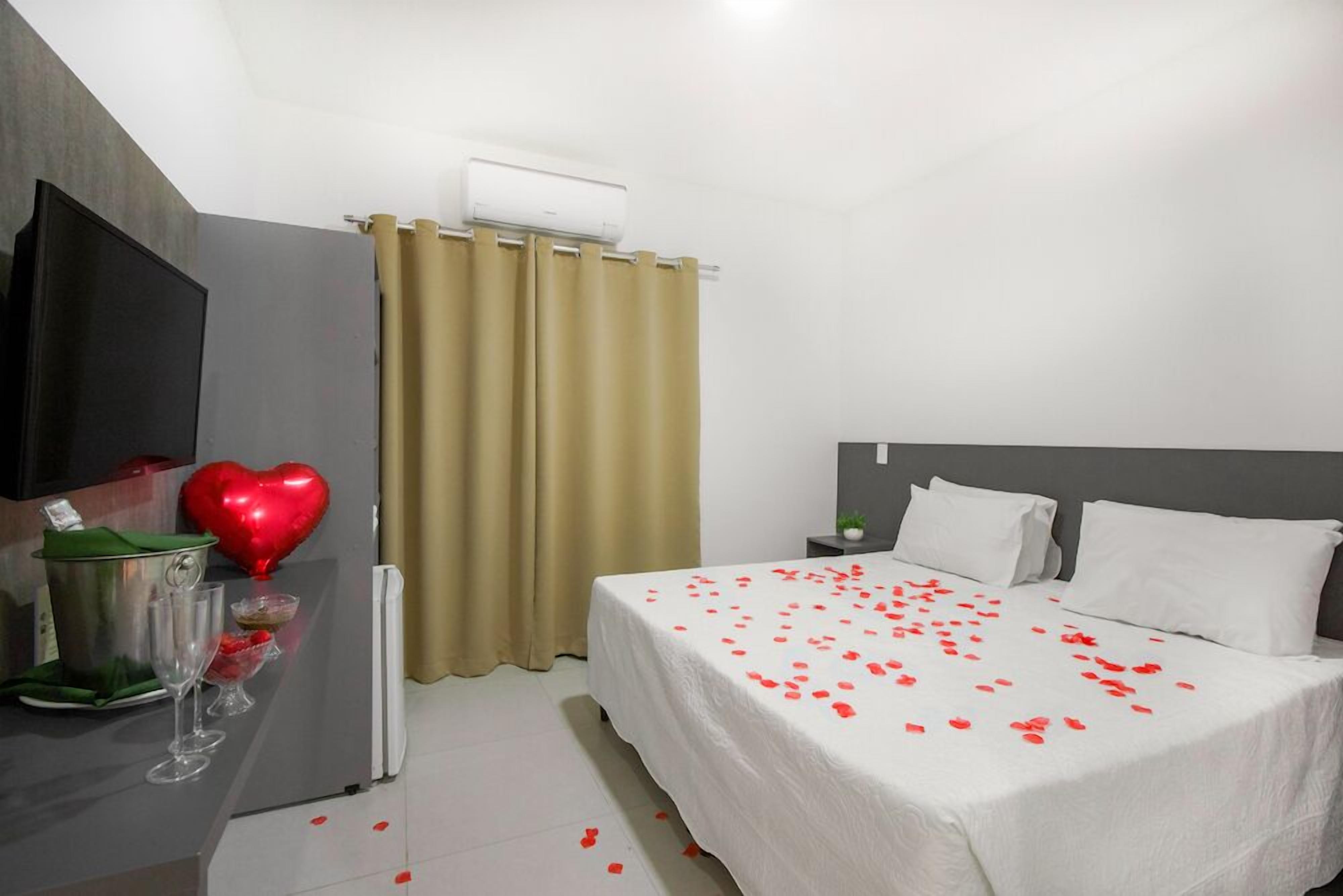 A hotel room with a bed, a TV, a minibar, and a curtain.