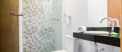 A modern bathroom with a glass shower enclosure, a white toilet, and a black countertop sink with a mirror.
