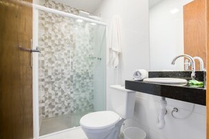 Un baño moderno con cabina de ducha de vidrio, inodoro blanco y lavamanos con encimera negra y espejo.