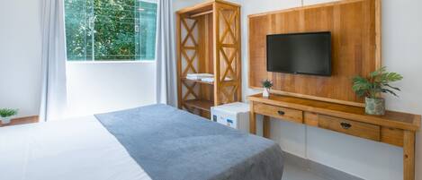 A modern hotel room with a large bed, a wooden desk with a TV, and a window with curtains.
