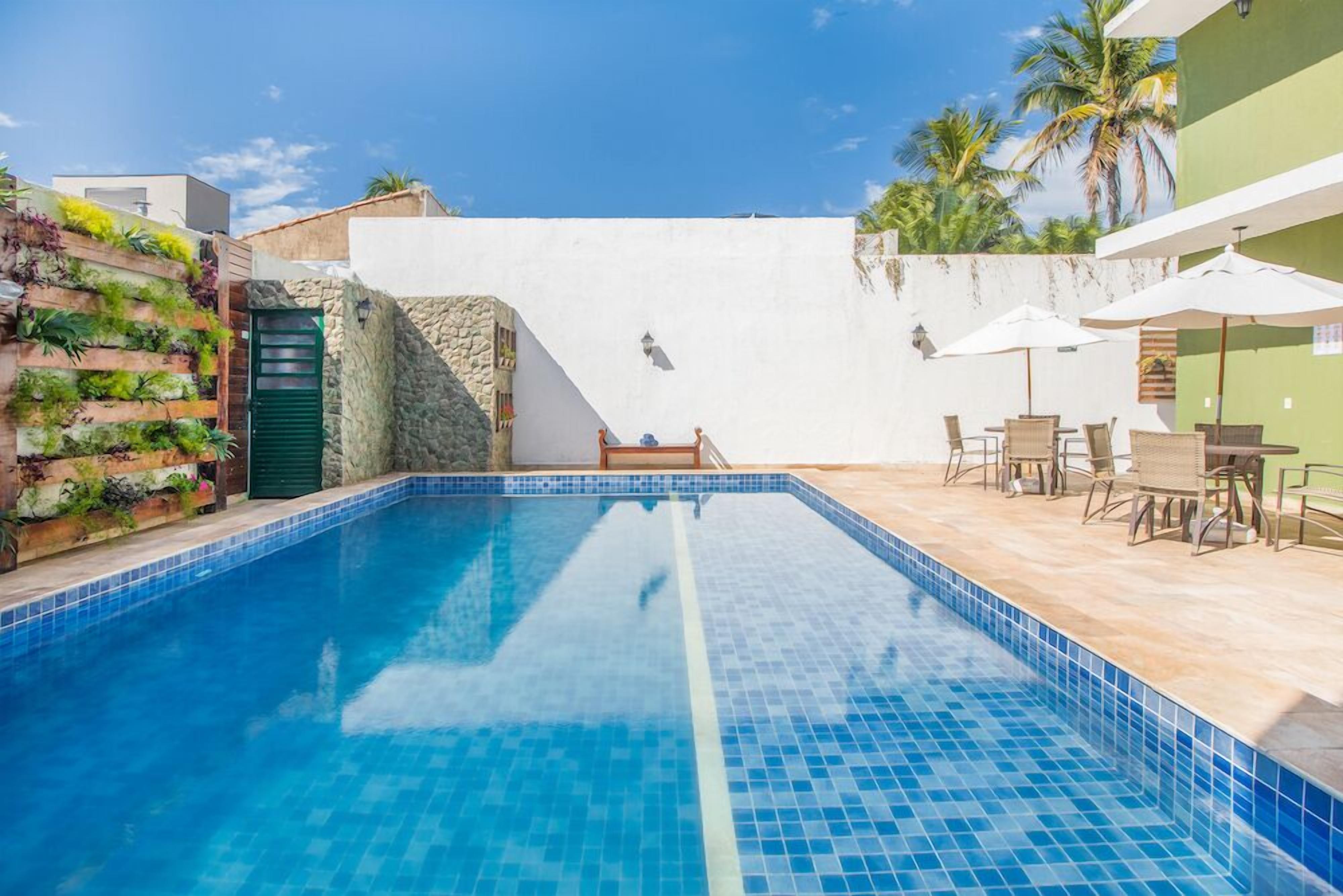 Una piscina con bordes de azulejos, una cubierta de madera y mobiliario exterior.