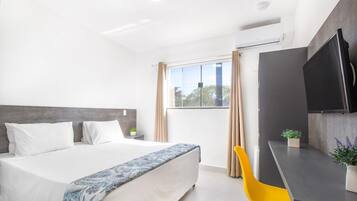 A modern hotel room with a large bed, a desk, a flat-screen TV, and a window with curtains.