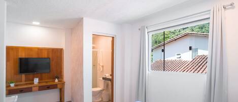Un dormitorio moderno con televisor, un escritorio de madera y un baño visible a través de una puerta abierta.