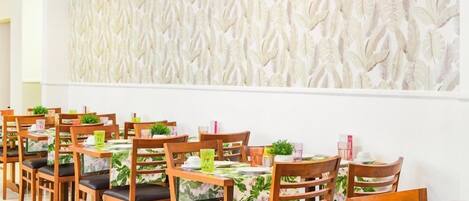 A dining area with wooden tables and chairs, each with a floral tablecloth.