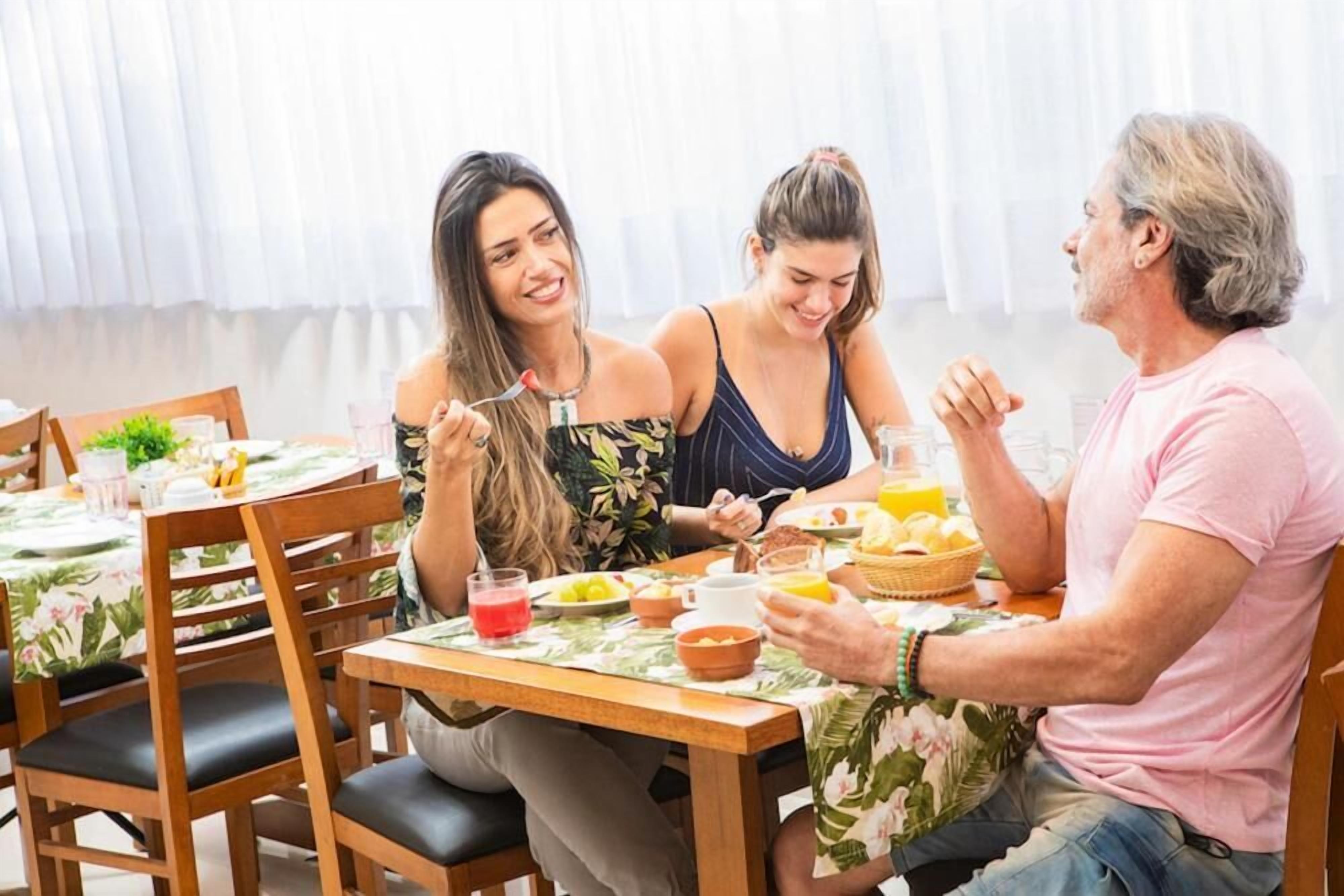 A dining area with wooden tables and chairs, a floral tablecloth, and a variety of breakfast foods and drinks.