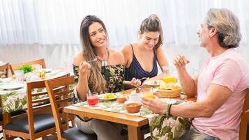 A dining area with wooden tables and chairs, a floral tablecloth, and a variety of breakfast foods and drinks.
